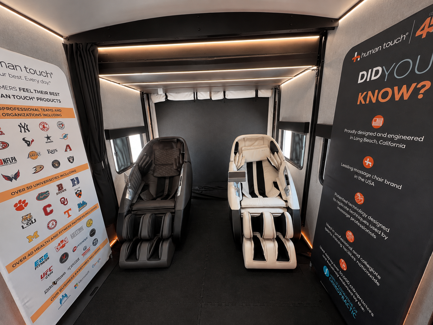 Interior of the Human Touch Recovery Lounge trailer with two premium massage chairs and branding banners