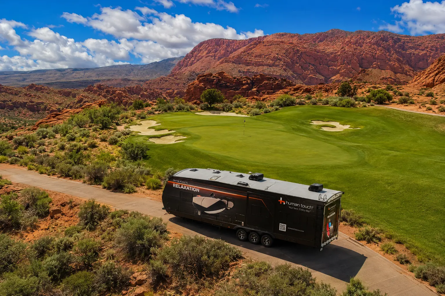 Aerial view of the Human Touch Recovery Lounge trailer parked on the Black Desert golf course with red rock mountains in the background